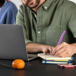 Estudiante universitario redactando notas en su cuaderno de estudio junto a una laptop abierta, aplicando técnicas de metacognición en un curso de aprender a aprender con IA gratis.